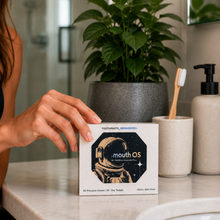 Hand placing a Mouth OS Mint Frost box on a marble bathroom counter beside a toothbrush